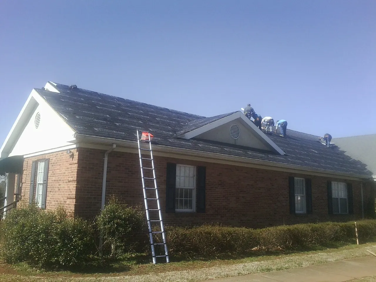Crew tearing shingles off a brick ranch roof with a ladder set — Metal Roof Repair work by our crew in West Lebanon